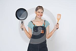 Young woman wearing kitchen apron cooking and holding pan and spatula isolated on white background