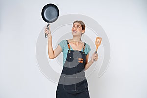 Young woman wearing kitchen apron cooking and holding pan and spatula isolated on white background