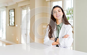 Young woman wearing medical coat at the clinic as therapist or doctor happy face smiling with crossed arms looking at the camera