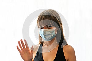 Young woman wearing medical face mask waving at camera