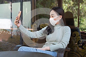 Young woman wearing medical mask making selfie or video call with smartphone at coffee shop