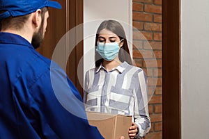 Young woman wearing medical mask receiving parcel from delivery man. Prevention of virus spread