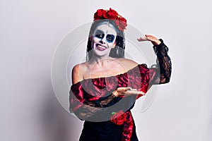 Young woman wearing mexican day of the dead makeup gesturing with hands showing big and large size sign, measure symbol
