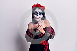 Young woman wearing mexican day of the dead makeup laughing nervous and excited with hands on chin looking to the side