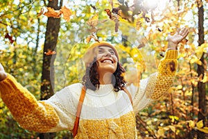 Young woman wearing an orange hat, sweater and small backpack throws up the leaves in the autumn forest. Female explores the