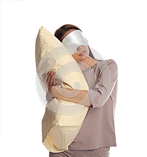 Young woman wearing pajamas and mask with pillow in sleepwalking state on white background