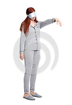 Young woman wearing pajamas, mask and slippers in sleepwalking state on white background