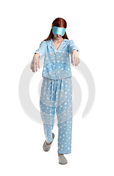 Young woman wearing pajamas, mask and slippers in sleepwalking state on white background
