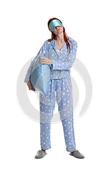 Young woman wearing pajamas and slippers with pillow in sleepwalking state on white background