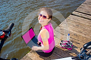 Young woman wearing in pink shirt sitting on the lake bridge using laptop computer