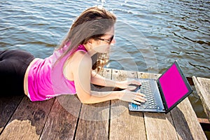 Young woman wearing in pink shirt sitting on the lake bridge using laptop computer