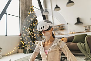 A young woman, wearing a pink sports outfit, practices yoga with a virtual reality headset near a Christmas tree