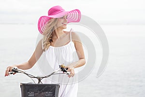 Young woman wearing pink sunhat walking with bicycle along beach