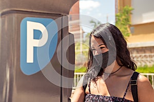 Young woman wearing protective mask using parking machine on the street