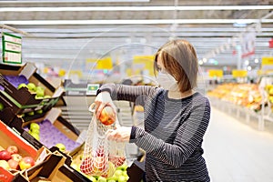 Young woman wearing protective medical face mask shopping in supermarket during coronavirus pneumonia outbreak