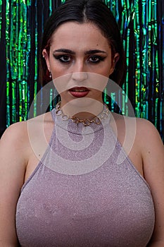 Young woman wearing purple halter neck dress posed in front of green sparkly curtains