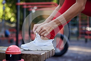 Young woman, wearing red fitness outfit, tying shoe laces on white sneakers. Process of fastening sport shoes. Close-up shot of