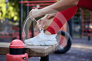 Young woman, wearing red fitness outfit, tying shoe laces on white sneakers. Process of fastening sport shoes. Close-up shot of
