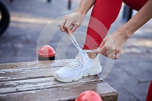 Young woman, wearing red fitness outfit, tying shoe laces on white sneakers. Process of fastening sport shoes. Close-up shot of