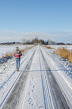 Young woman wearing red Norwegian jumper going for a winter walk with dog on snow covered road on a beautiful sunny day