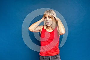 Young woman wearing red shirt standing over blue background with hand on head. Omg, shoked, surprised girl photo