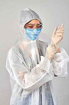 Young woman wearing respiratory mask and putting on white medical rubber gloves.