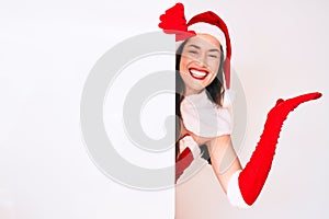 Young woman wearing santa claus costume holding blank empty banner celebrating victory with happy smile and winner expression with