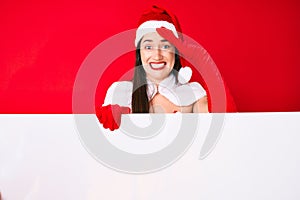 Young woman wearing santa claus costume holding blank empty banner stressed and frustrated with hand on head, surprised and angry