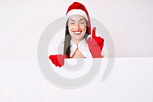 Young woman wearing santa claus costume holding blank empty banner surprised with an idea or question pointing finger with happy