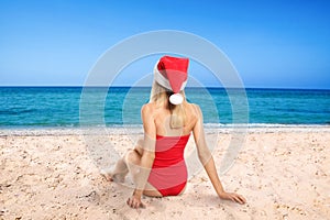 Young woman wearing Santa Claus hat on beach near sea, back view. Christmas vacation