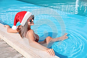 Young woman wearing Santa Claus hat in swimming pool. Christmas vacation