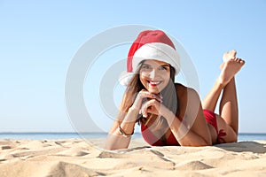 Young woman wearing Santa hat and bikini on beach. Christmas vacation
