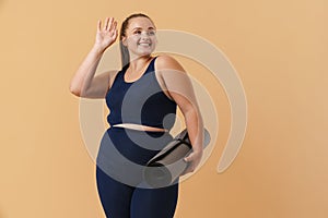 Young woman wearing sport suit gesturing while posing with fitness mat