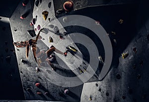 Young woman wearing sportswear practicing rock-climbing on a wall indoors