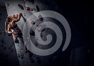 Young woman wearing sportswear practicing rock-climbing on a wall indoors