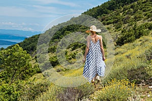 Young woman wearing striped summer dress and straw hat walking among super bloom of wildflowers, relaxing while enjoing