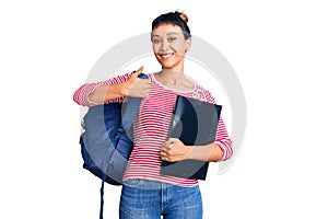 Young woman wearing student backpack holding binder smiling happy and positive, thumb up doing excellent and approval sign