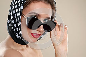 Young woman wearing stylish sunglasses and headscarf on background