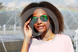 young woman wearing sunglasses with perfect teeth and dark clean skin having rest outdoors