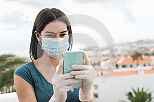 Young woman wearing surgical face mask using mobile smartphone on home terrace - Girl in quarantine having fun with new technology