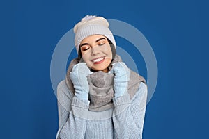 Young woman wearing sweater, gloves, scarf and hat on blue background. Winter season