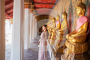 Young woman wearing Thai dress with accessories carrying a bag at Wat Arun Ratchawararam where many Buddha statues are row It is a