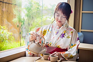 Young woman wearing traditional kimono sitting in a Japanese style house pouring tea to drink