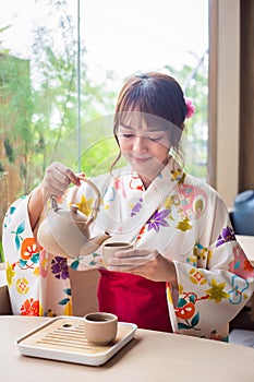 Young woman wearing traditional kimono sitting in a Japanese style house pouring tea to drink