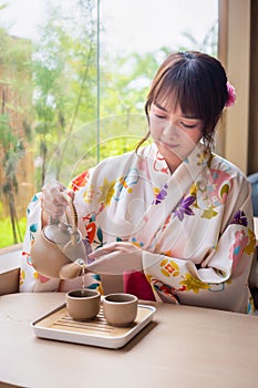 Young woman wearing traditional kimono sitting in Japanese style house with tea set