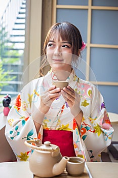 Young woman wearing traditional kimono sitting in Japanese style house with tea set