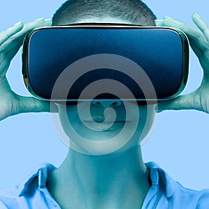 Young woman wearing virtual reality goggles. Woman wearing VR glasses over blue background. VR experience concept, close up. photo