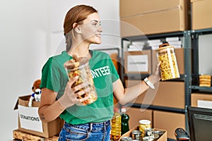 Young woman wearing volunteer uniform holding pasta jar at charity center