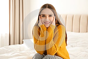 Young woman wearing warm sweater on bed at home. Winter season