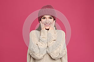 Young woman wearing warm sweater and hat on crimson background. Winter season